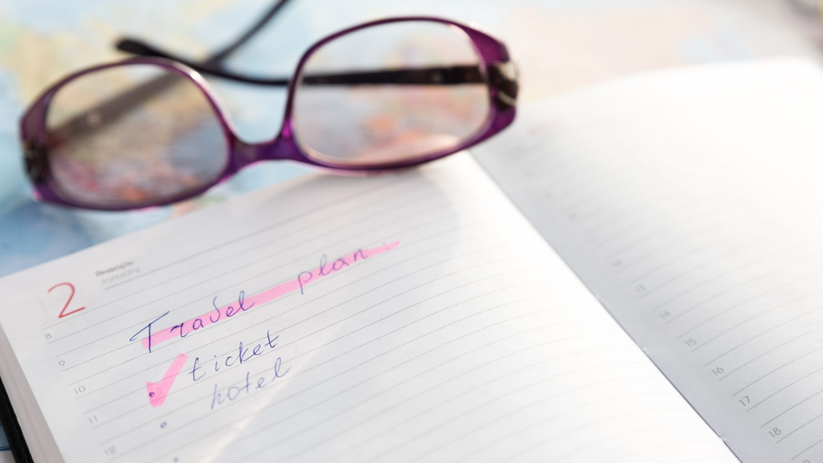 Ein handschriftlicher Reiseplan im Notizbuch, daneben eine Lesebrille